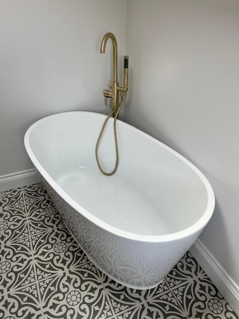 Freestanding bath with floor-mounted gold tap and patterned floor tiles